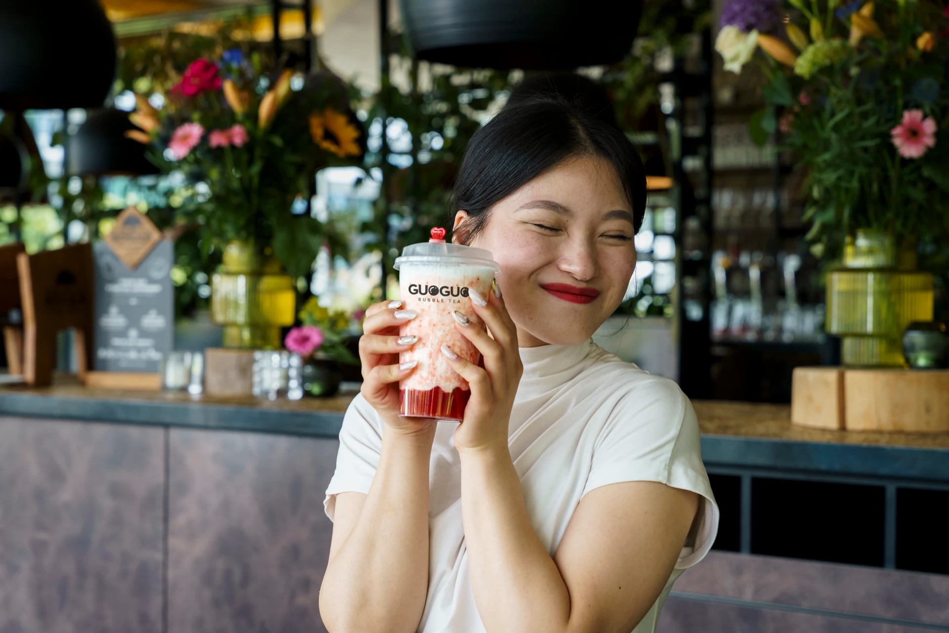 Een glimlachende vrouw houdt een GUOGUO bubble tea naast haar gezicht