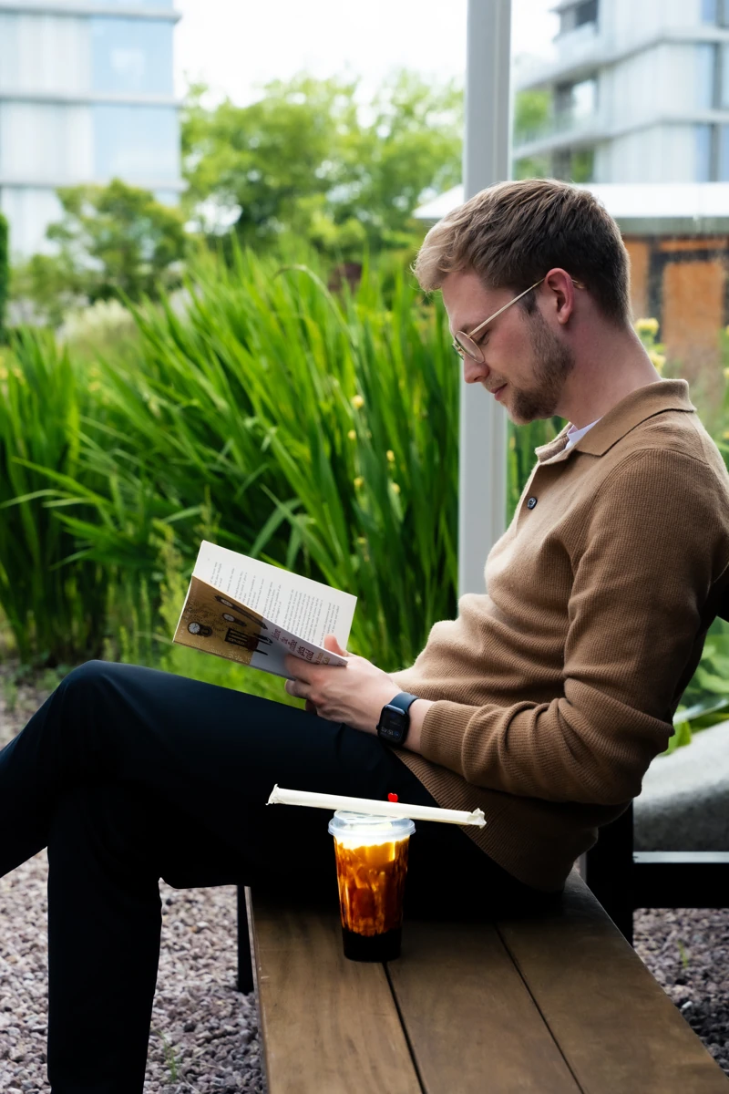 Een man leest een boek met bubble tea naast zich